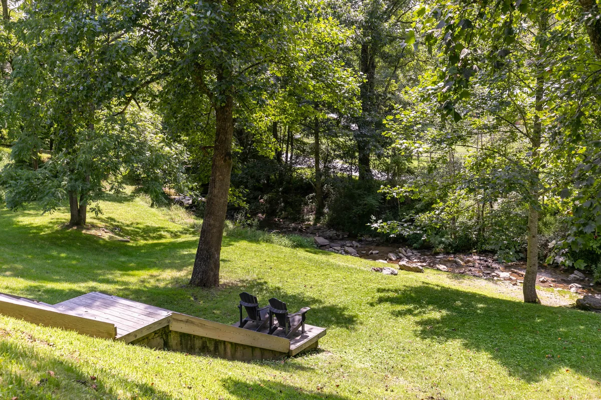 A tranquil view of two black chairs set beside a gentle stream surrounded by vibrant, lush greenery. The scene radiates peace and invites families to relax, read, or picnic while enjoying the sounds and sights of nature.
