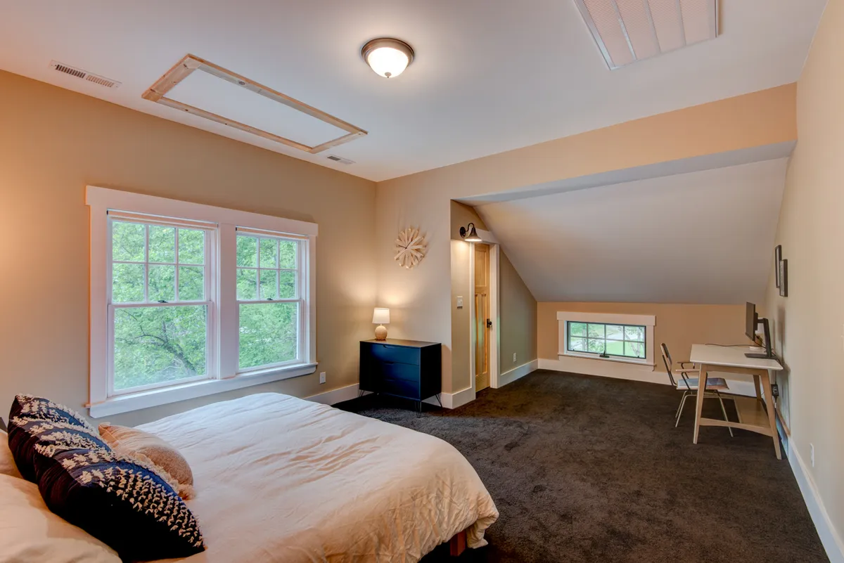 A serene bedroom with a comfortable bed, crisp linens, a work desk positioned near the window, and plenty of natural light. The setting is ideal for remote work or restful sleep, embracing both productivity and relaxation.
