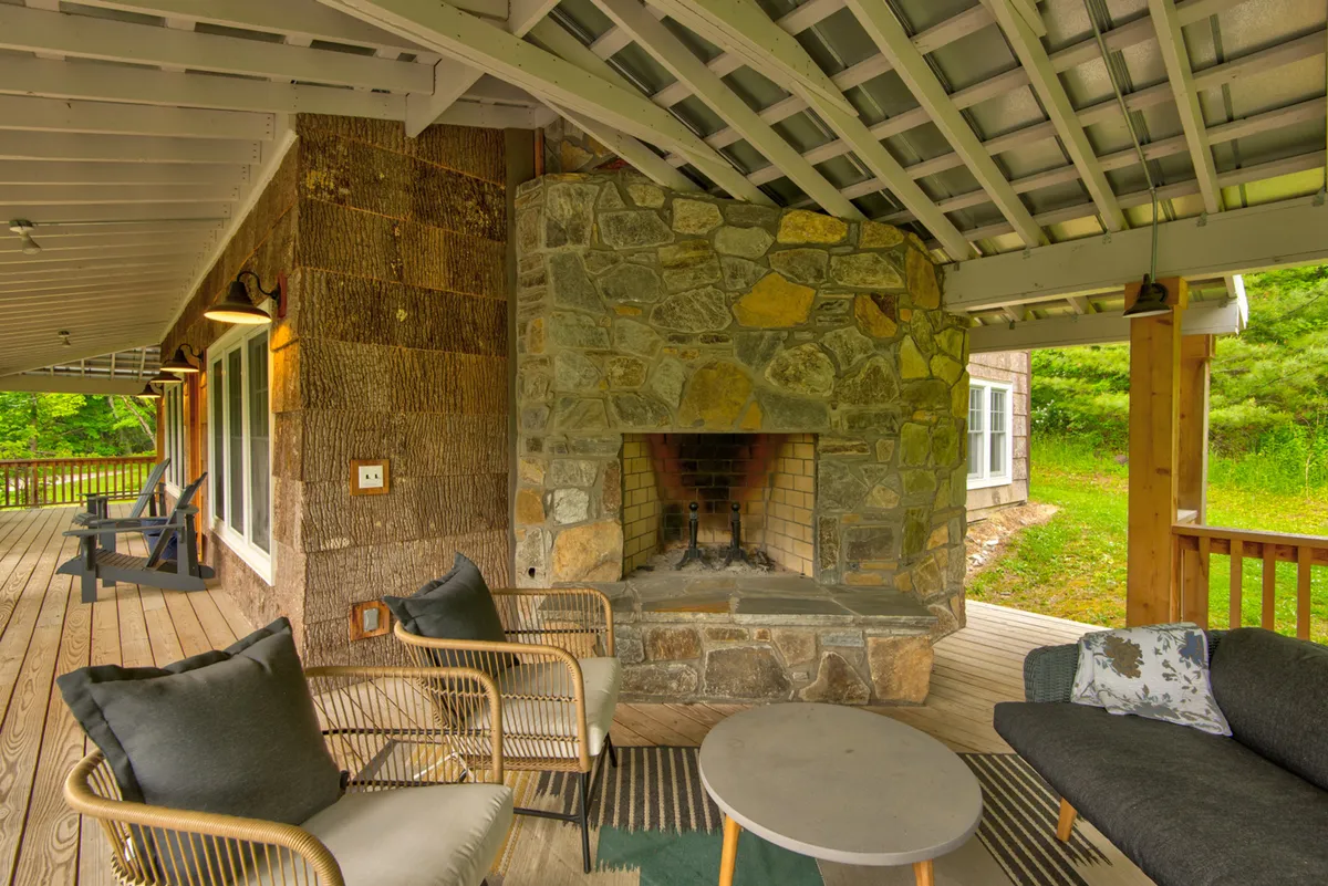 A cozy, welcoming outdoor living area with a stone fireplace, comfortable seating, and a wooden deck overlooking natural views. The space is ideal for intimate gatherings, relaxing by the fire, or stargazing at night.