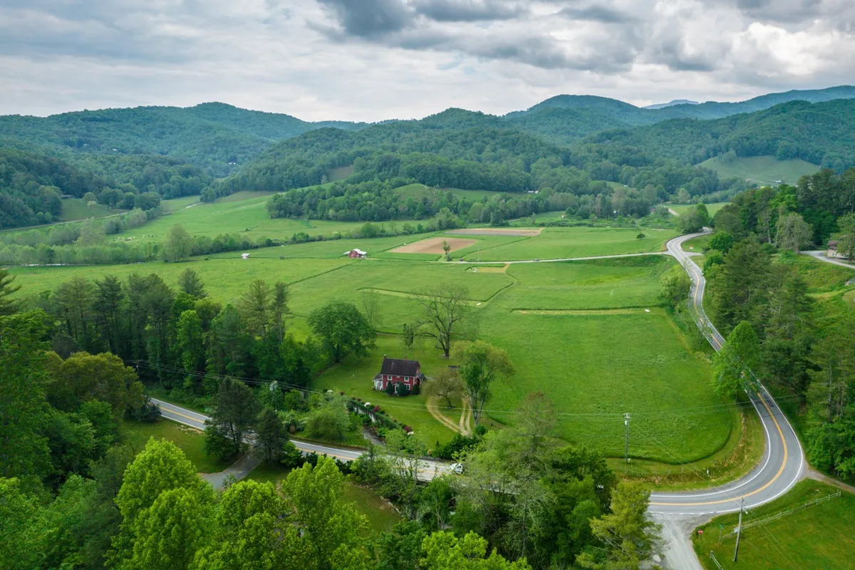 A panoramic view of the local landscape featuring rolling hills, a farmhouse, a curving country road, and a distant barn. The scene evokes tranquility and a connection to Valle Crucis’s rural charm, inviting guests to explore the area’s history and natural beauty on gentle strolls.