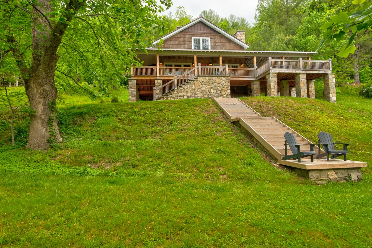 An exterior shot capturing the house with stone steps leading up to it and Adirondack chairs set outdoors, surrounded by nature. The scene highlights the connection to the environment and the relaxation opportunities the property offers.