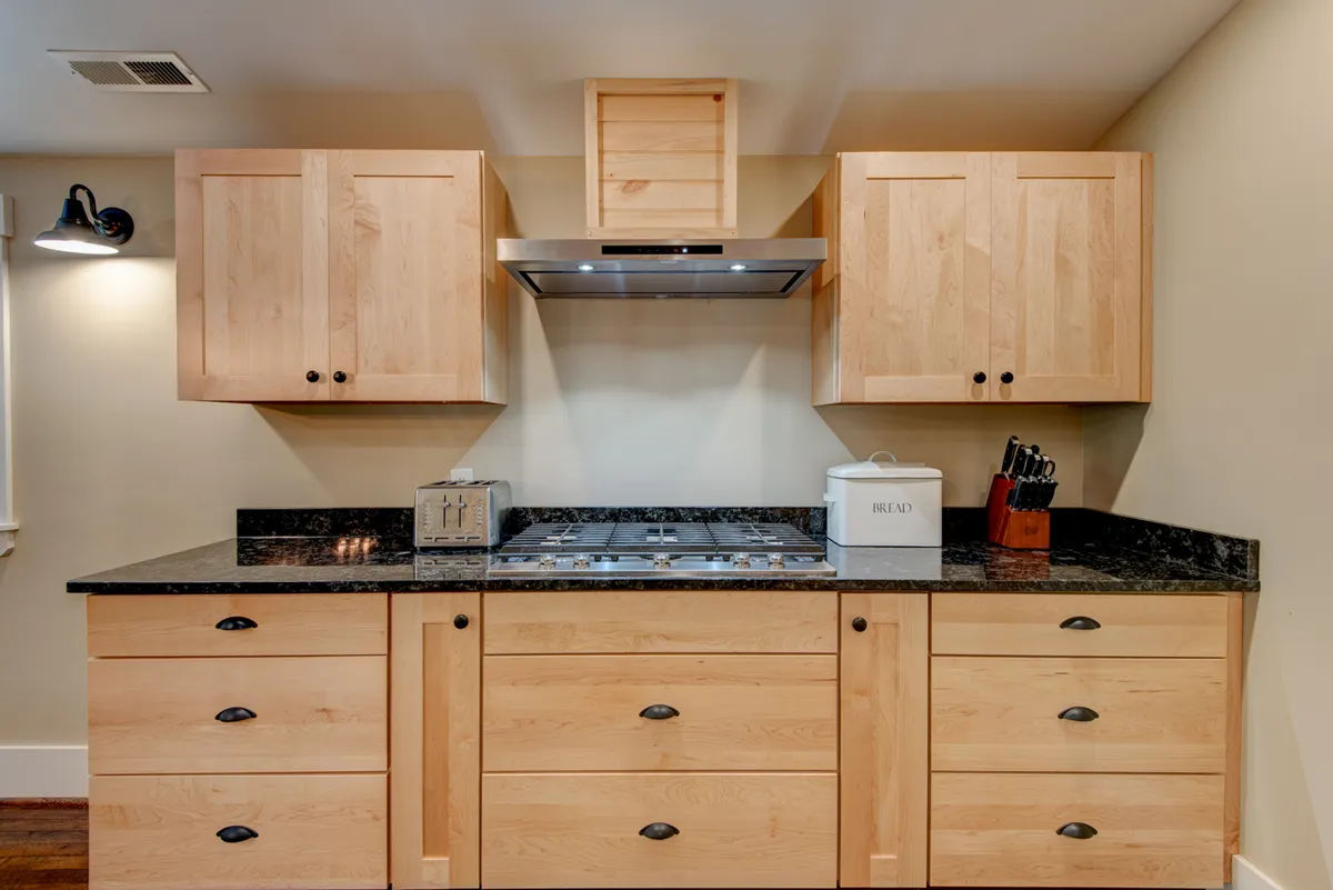 A modern yet charming kitchen is featured with granite countertops, wooden cabinetry, and a stainless steel extractor hood. The space feels both functional and stylish, ready for casual breakfasts or elaborate feasts.