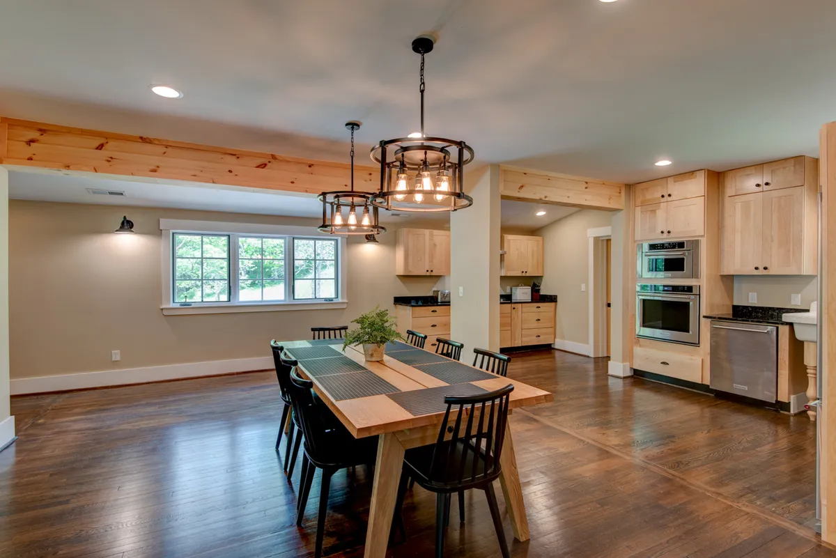 This image centers on a spacious dining table beneath elegant chandeliers, with the gourmet kitchen’s cabinetry visible in the background. The table is set for a family dinner or board game night, and the ambiance is warm and welcoming.