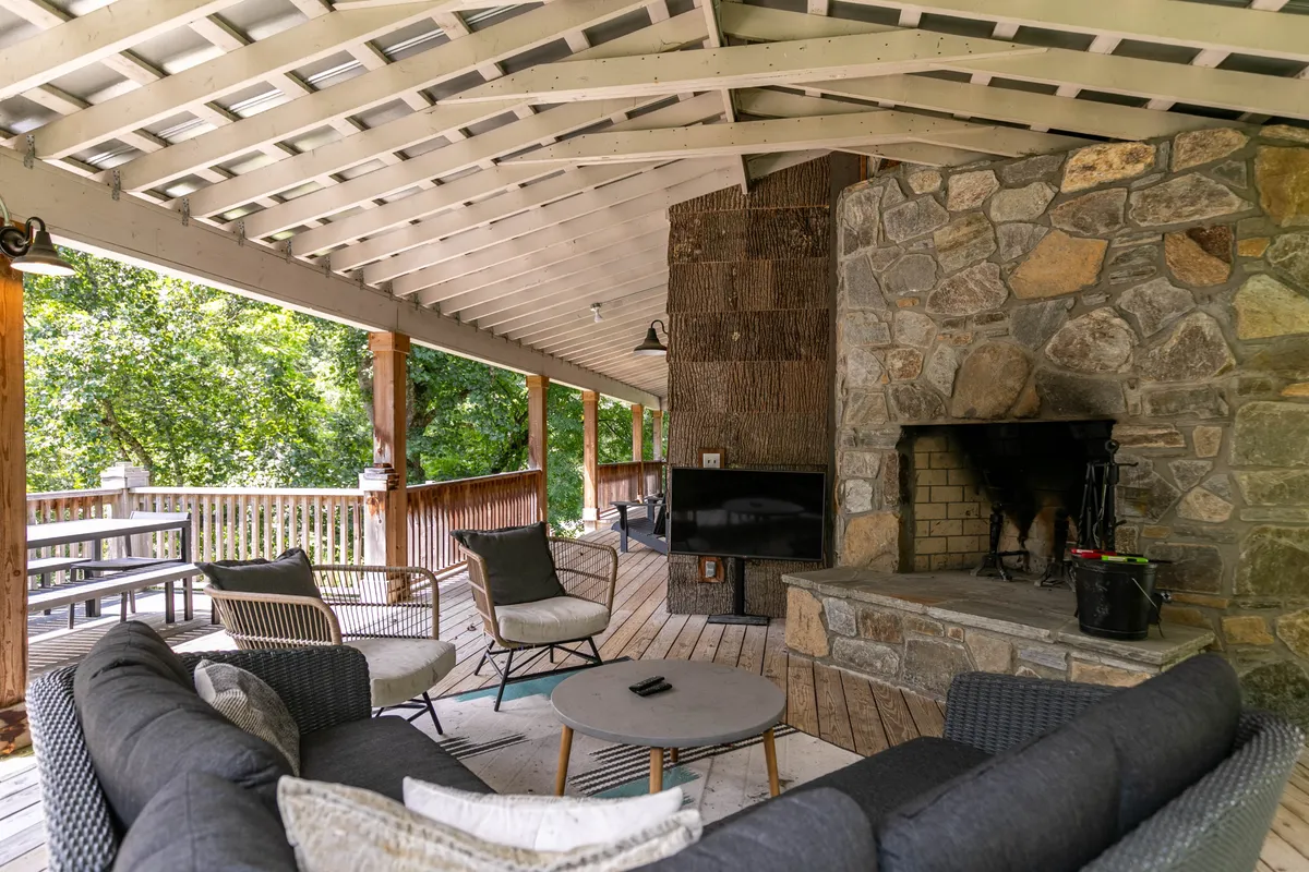 The image showcases a cozy outdoor seating area on a wooden deck, complete with a stone fireplace and lush greenery in the background. Comfortable chairs are positioned to enjoy the warmth of the fire and the surrounding natural beauty, embodying the ideal space for evening relaxation or streaming favorite shows outdoors as described in the section.