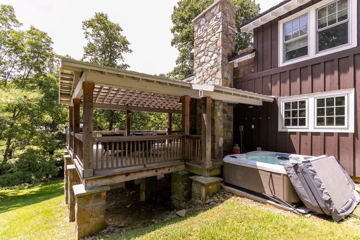 A spacious, covered deck featuring a hot tub, stone chimney, and plenty of room for outdoor dining or lounging. The setting is both relaxed and social, with the hot tub as a focal point and surrounded by scenic views.
