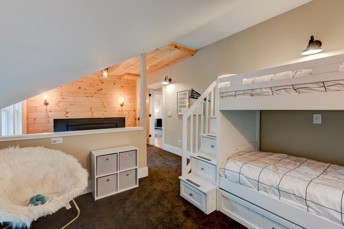 A playful, family-friendly room with a sturdy bunk bed, a cozy chair, a wooden accent wall, and a small staircase. The setting exudes fun and comfort, making it perfect for children or multi-generational sleepovers.