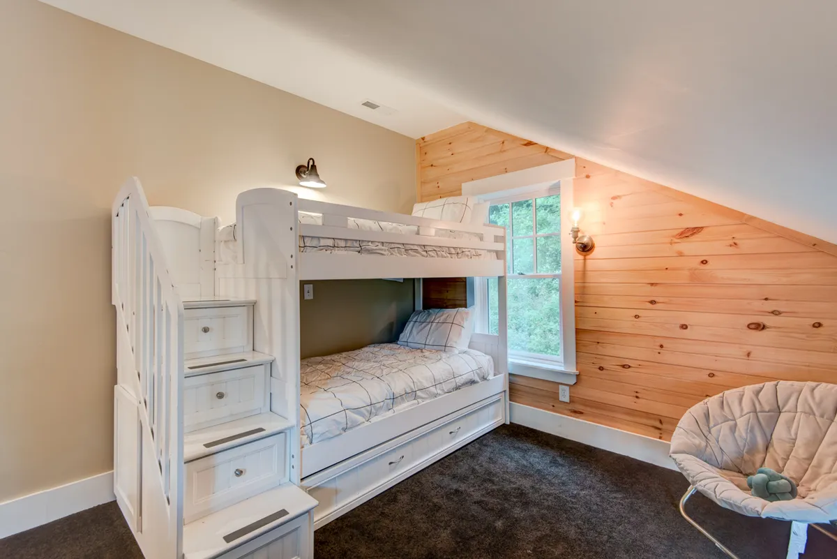 This interior image showcases a flexible bonus room with a bunk bed, large window with views, and an accent chair. The space feels welcoming and playful, ideal for children to sleep, play games, or enjoy movie nights together.