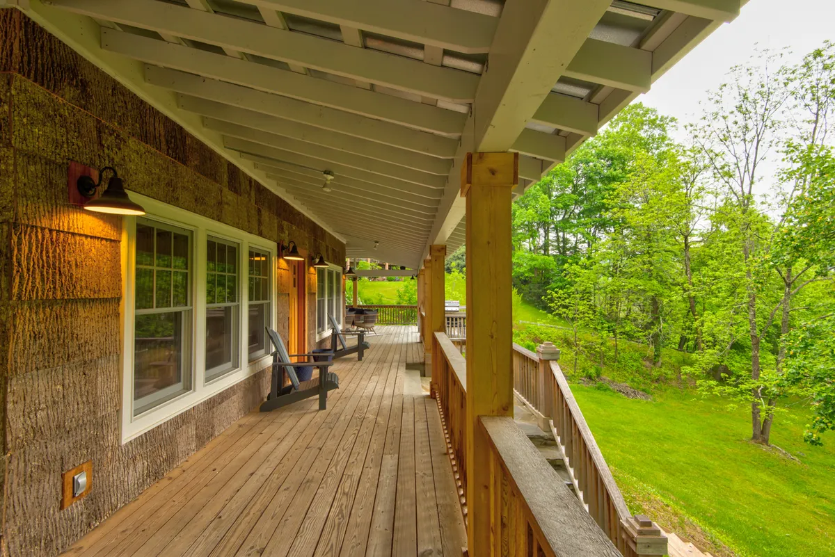 This image presents a wide wooden deck with outdoor seating, overlooking a green landscape and framed by large windows. The open-air setup offers an inspiring view and multiple options for working or unwinding, representing both productivity and relaxation in a scenic mountain setting.